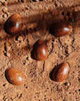 "Œufs de Pâques en chocolat bio disposés sur une surface recouverte de cacao en poudre. Leur texture lisse et brillante contraste avec l’aspect brut du cacao, créant une mise en scène naturelle et gourmande. Chocolat artisanal, idéal pour les fêtes de Pâques.