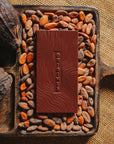 Tablette de chocolat noir Origines Chocolate Makers 100 % de cacao provenant du Liberia, entourée de fèves de cacao et de cabosses sur un fond en toile de jute.