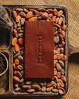Tablette de chocolat noir au café  Origines Chocolate Makers 70 % de cacao provenant de Colombie, entourée de fèves de cacao, de cabosses et d'un bol contenant du café sur un fond en toile de jute.