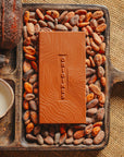Tablette de chocolat au lait Origines Chocolate Makers, 38 % de cacao provenant de São Tomé, entourée de fèves de cacao, de cabosses et d'un bol contenant du lait sur un fond en toile de jute.