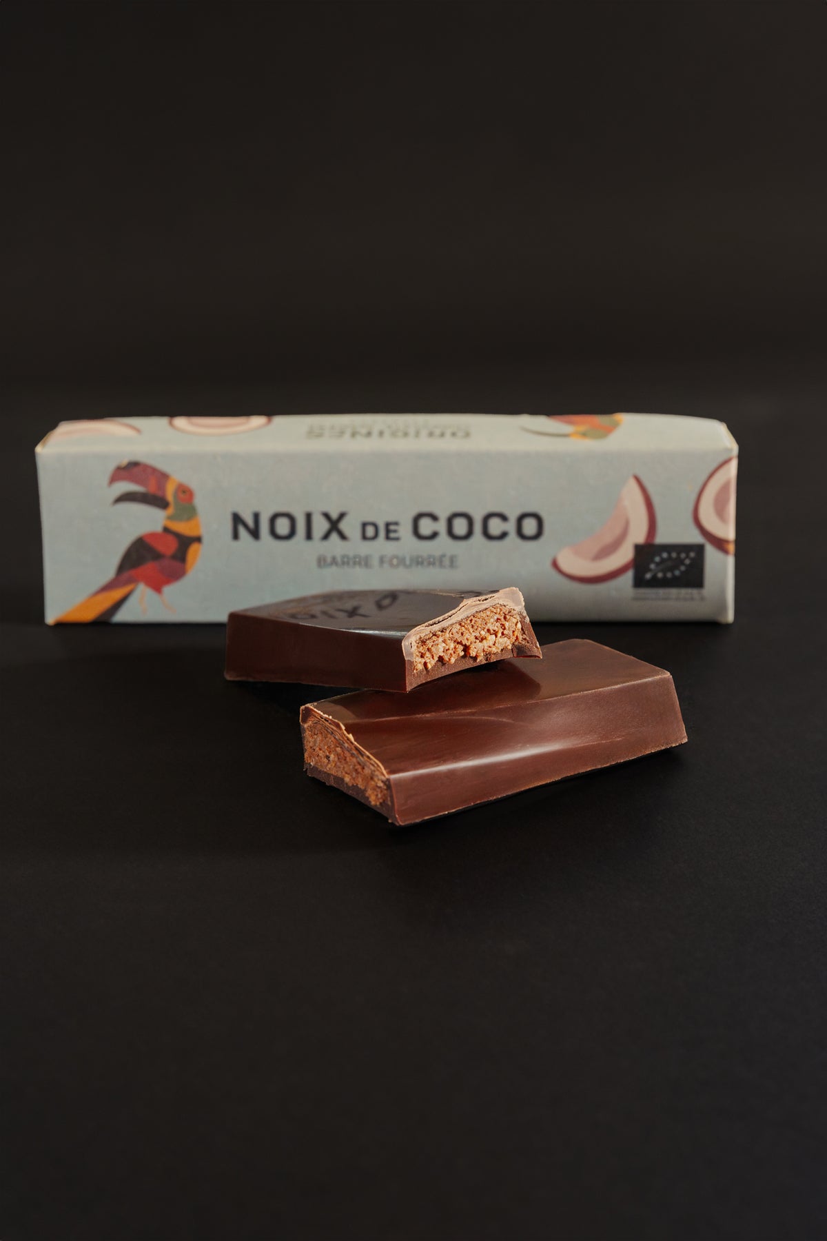 Barre chocolatée fourrée à la noix de coco avec un emballage marqué 'Noix de coco', sur fond noir.