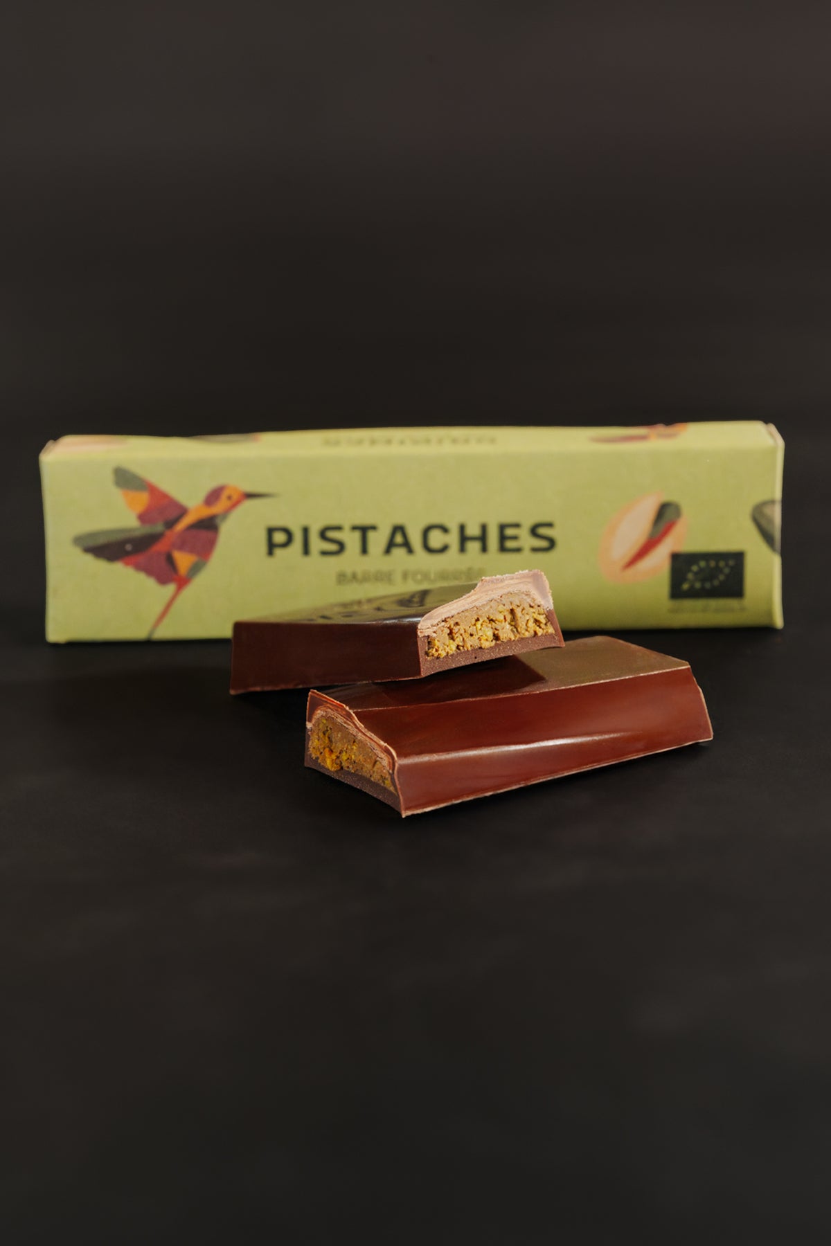 Barre chocolatée fourrée à la pistache avec un emballage marqué 'Pistaches', sur fond noir.