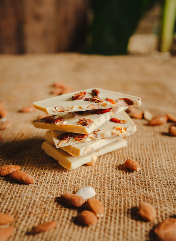 Morceaux de chocolat blanc aux amandes empilés sur une toile de jute, avec des amandes dispersées autour, en arrière-plan naturel.